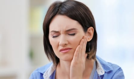 Woman in blue blouse holding her cheek in pain