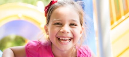 Little girl in pink shirt smiling at a playground