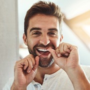 Closeup of smiling patient flossing their teeth