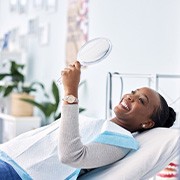 Woman smiling at reflection in handheld mirror