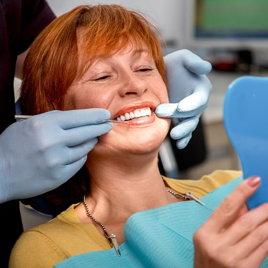 Woman looking at her smile in mirror at the dental office