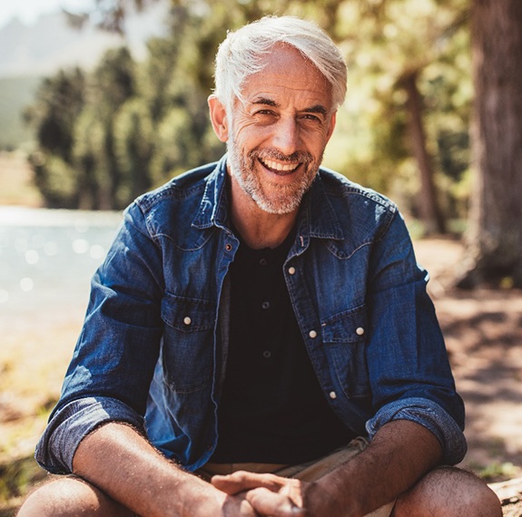An older man sitting outside by the lake and smiling after receiving CEREC in Fairfax