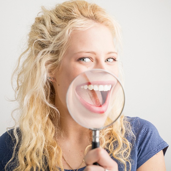 A young woman smiling wide while holding a magnifying glass up to her mouth