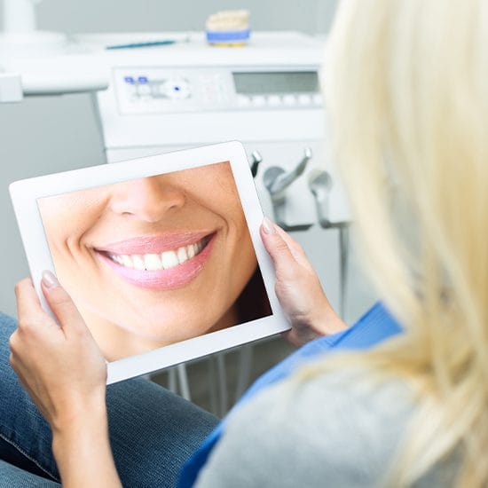 Woman looking at virtual smile design image on tablet computer