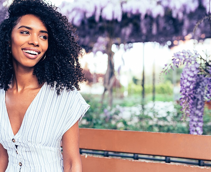 Smiling woman sitting on a bench outdoors near purple flowers