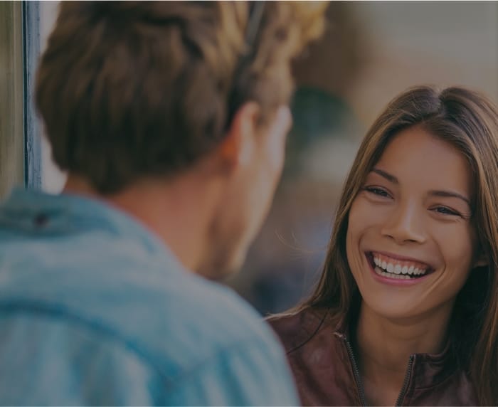 Woman in brown leather jacket smiling at man in denim shirt