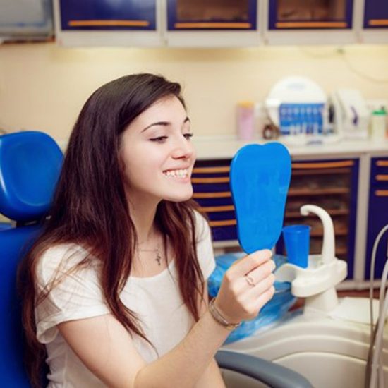 young woman seeing her new dental crown in Fairfax in a mirror 