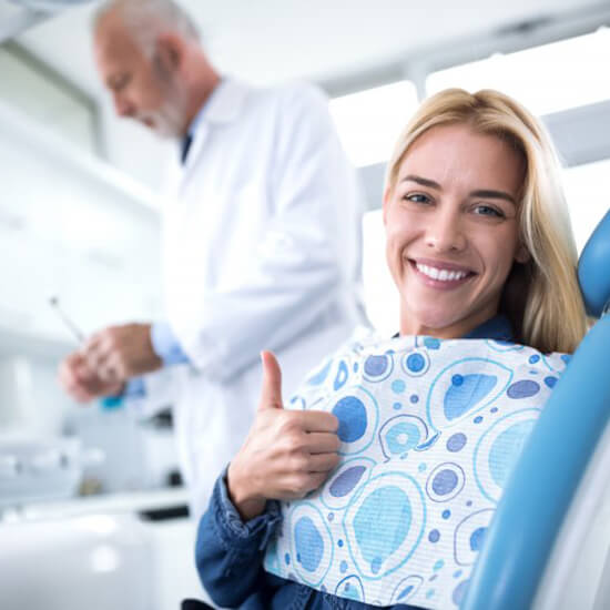 smiling woman giving thumbs up in dental chair 
