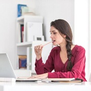 woman sitting at a desk and chewing on a pencil