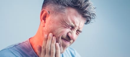 Man in blue shirt holding his jaw in pain