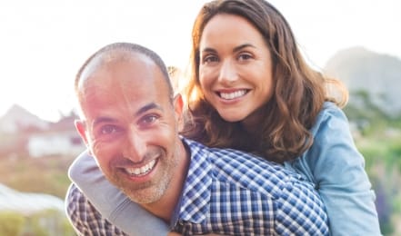 Smiling woman holding smiling man from behind outdoors