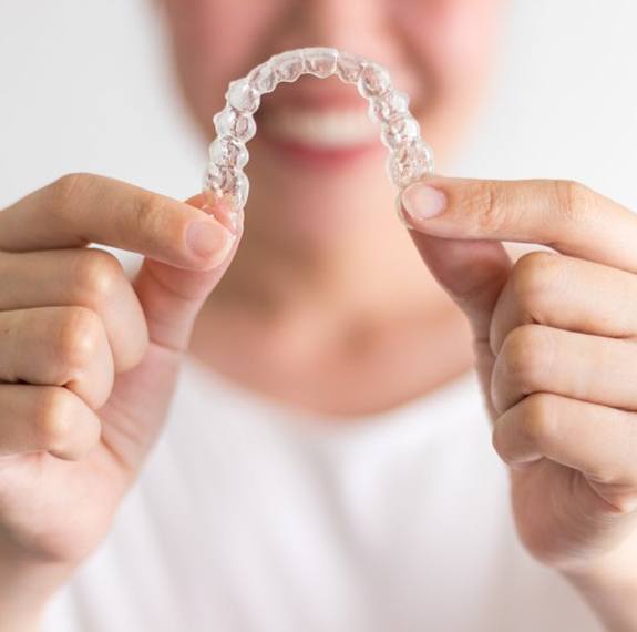 Closeup of smiling woman holding out Invisalign in Fairfax