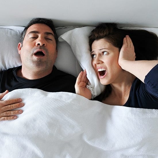Woman covering her ears next to snoring man