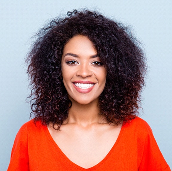 A young woman in a red blouse smiles after receiving veneers in Fairfax