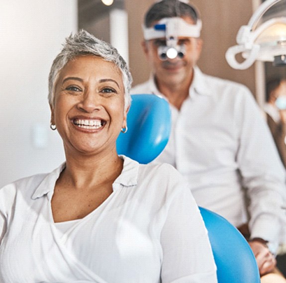 Woman in white shirt smiling while sitting in dentist's treatment chair