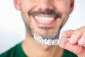 Man smiling while holding Invisalign clear aligner